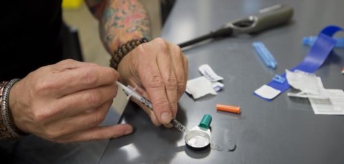 Image of drug paraphernalia on a table and someone filling a syringe 